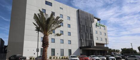 A modern hotel with a flat facade, multiple parking spaces, and a palm tree in the foreground.