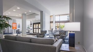 A modern lobby with a sofa, chairs, a lamp, and a sign about a king permit. - Harbor Towers 1st Fl. West Facing (Siesta Key)