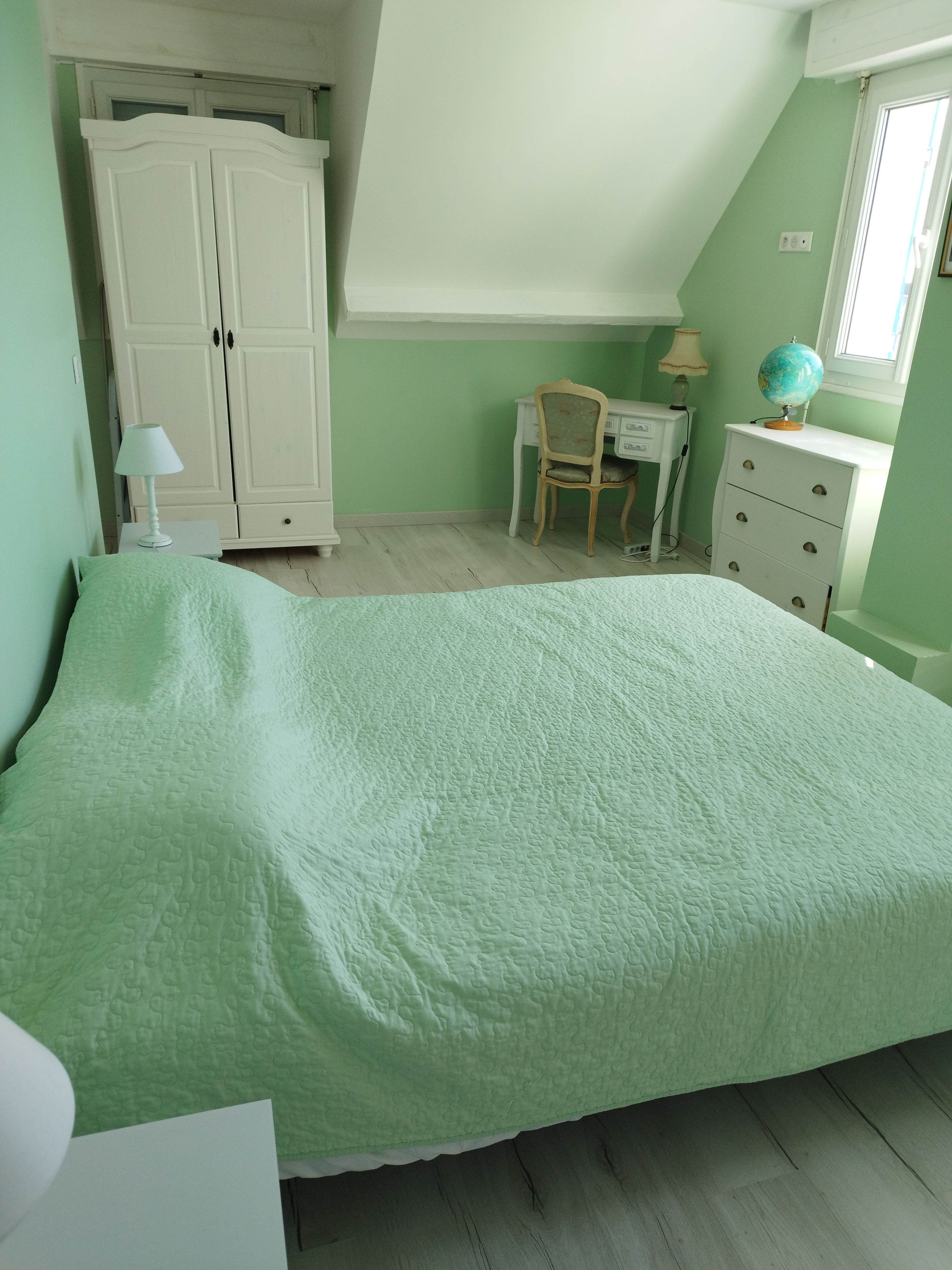 A bedroom with a bed, a desk, a chair, a wardrobe, and a globe on a dresser.