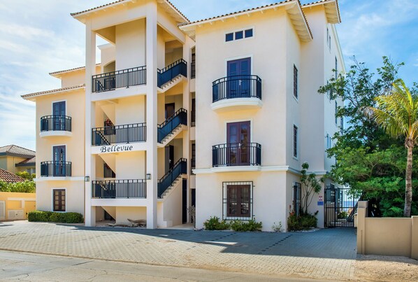 Un immeuble résidentiel à plusieurs étages, doté de balcons, d’une enseigne indiquant « Bellevue » et d’un espace d’entrée pavé.