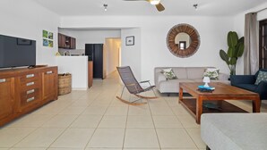 Un salon comprenant un canapé, une table basse, un téléviseur, un meuble en bois, un fauteuil à bascule et un ventilateur de plafond.