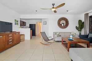 Un salon comprenant un canapé, une table basse, un téléviseur, un meuble en bois, un fauteuil à bascule et un ventilateur de plafond.