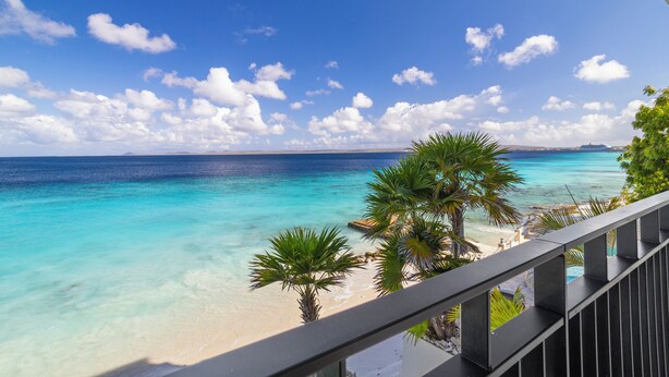 Une vue dégagée sur une plage aux eaux turquoise, bordée de palmiers et dotée d’une balustrade.