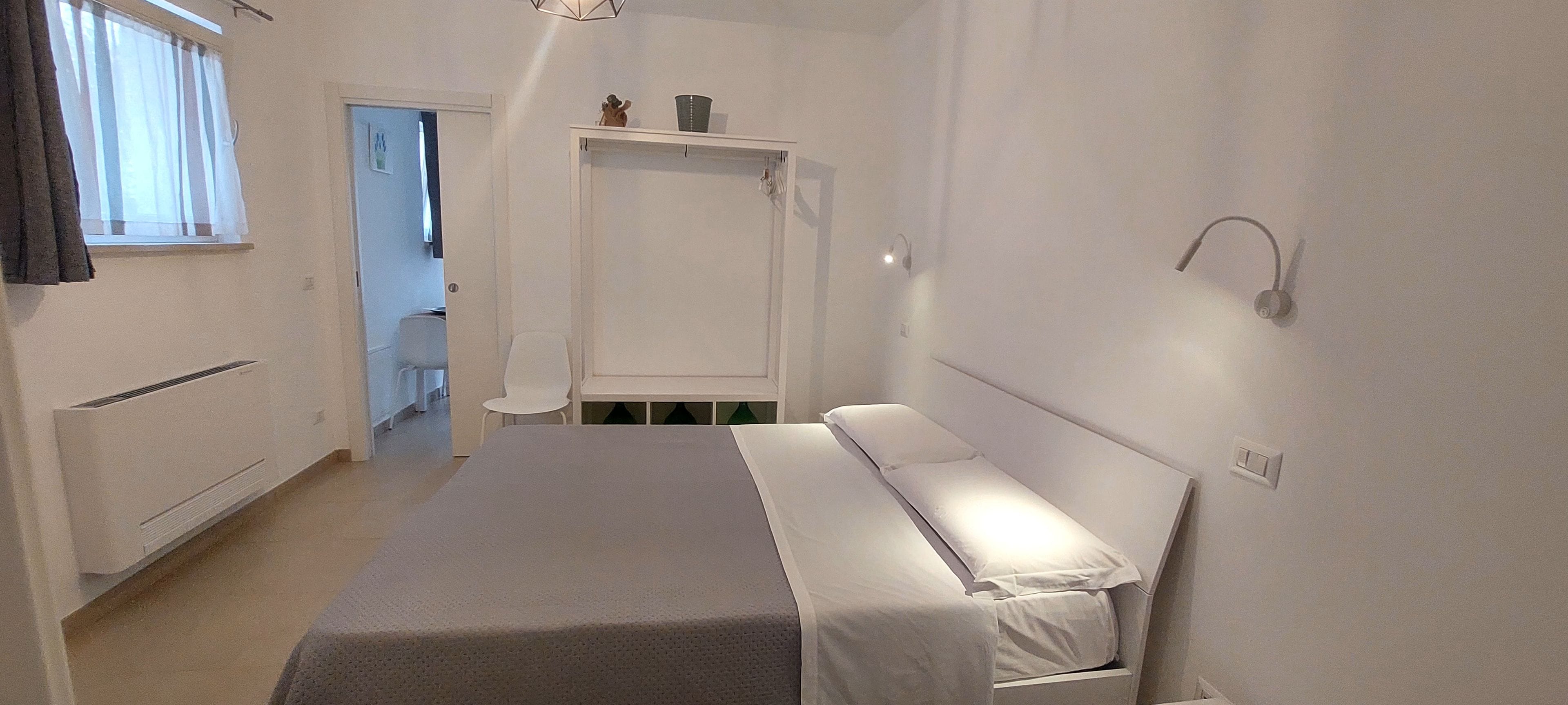 A narrow hotel room with a single bed, a small table, and a wardrobe.