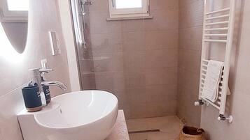 Un bany modern amb un lavabo gran, un espai de banyera amb envidriament i una finestra petita.
