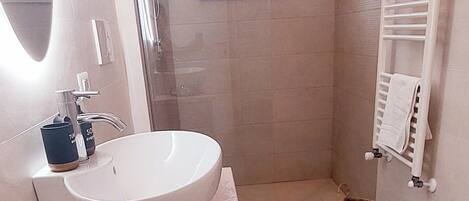 A modern bathroom with a large sink, a glass shower enclosure, and a small window.
