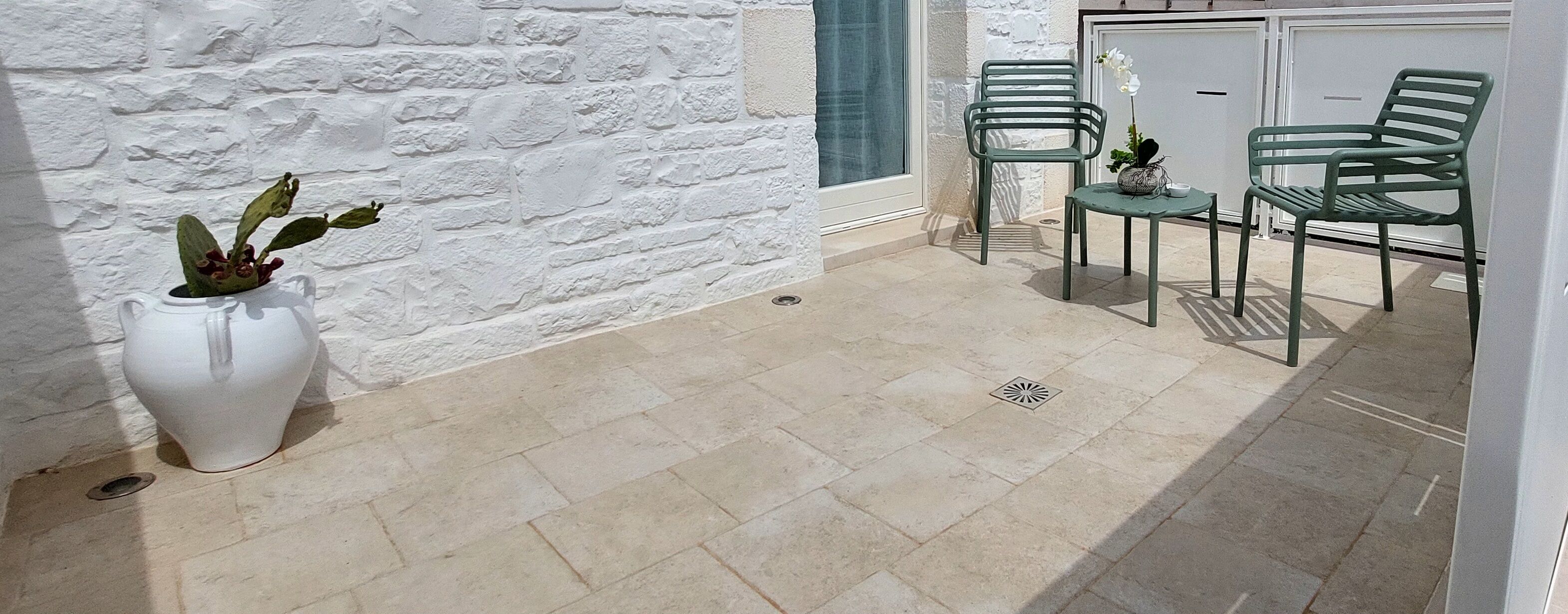 A patio area with a white stone wall, a tiled floor, and a seating arrangement with two chairs and a small table.