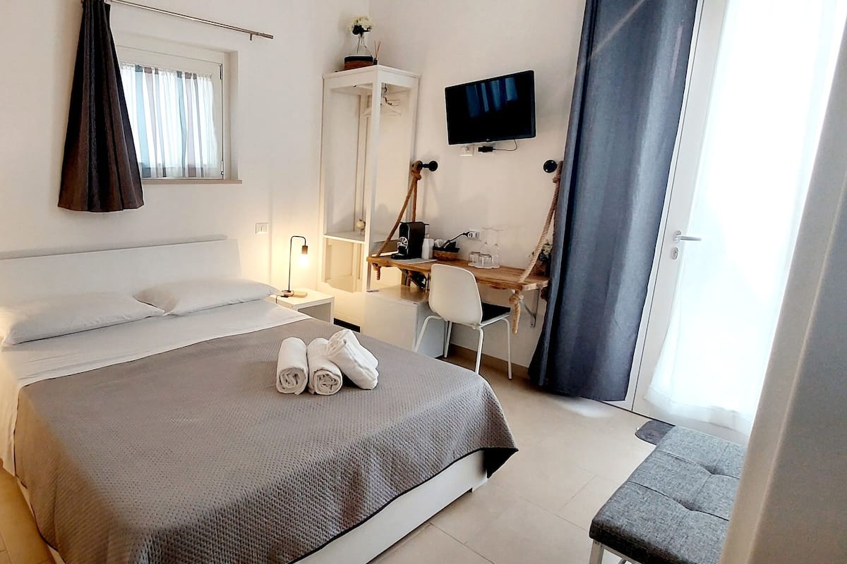 Ett sovrum med en säng, sängbord, ett skrivbord, en stol, en tv och ett fönster med gardiner.