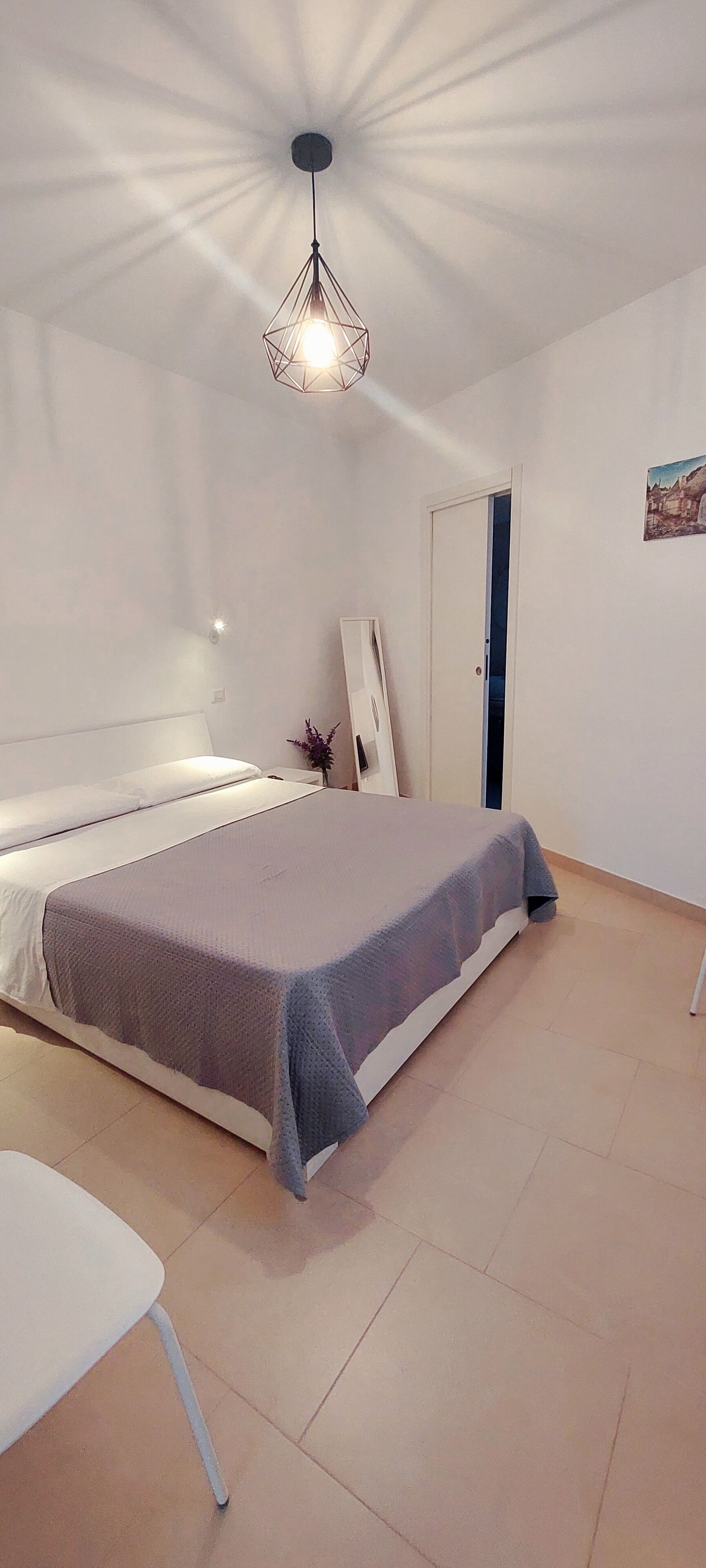 A bedroom with a bed, a chair, a ceiling light, and a door.