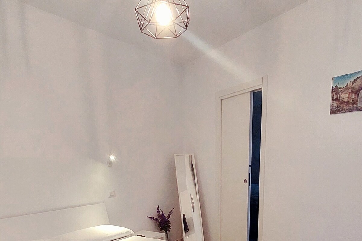 Un dormitorio con cama, una silla, una lámpara en el techo y una puerta.