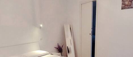 A bedroom with a bed, a chair, a ceiling light, and a door.