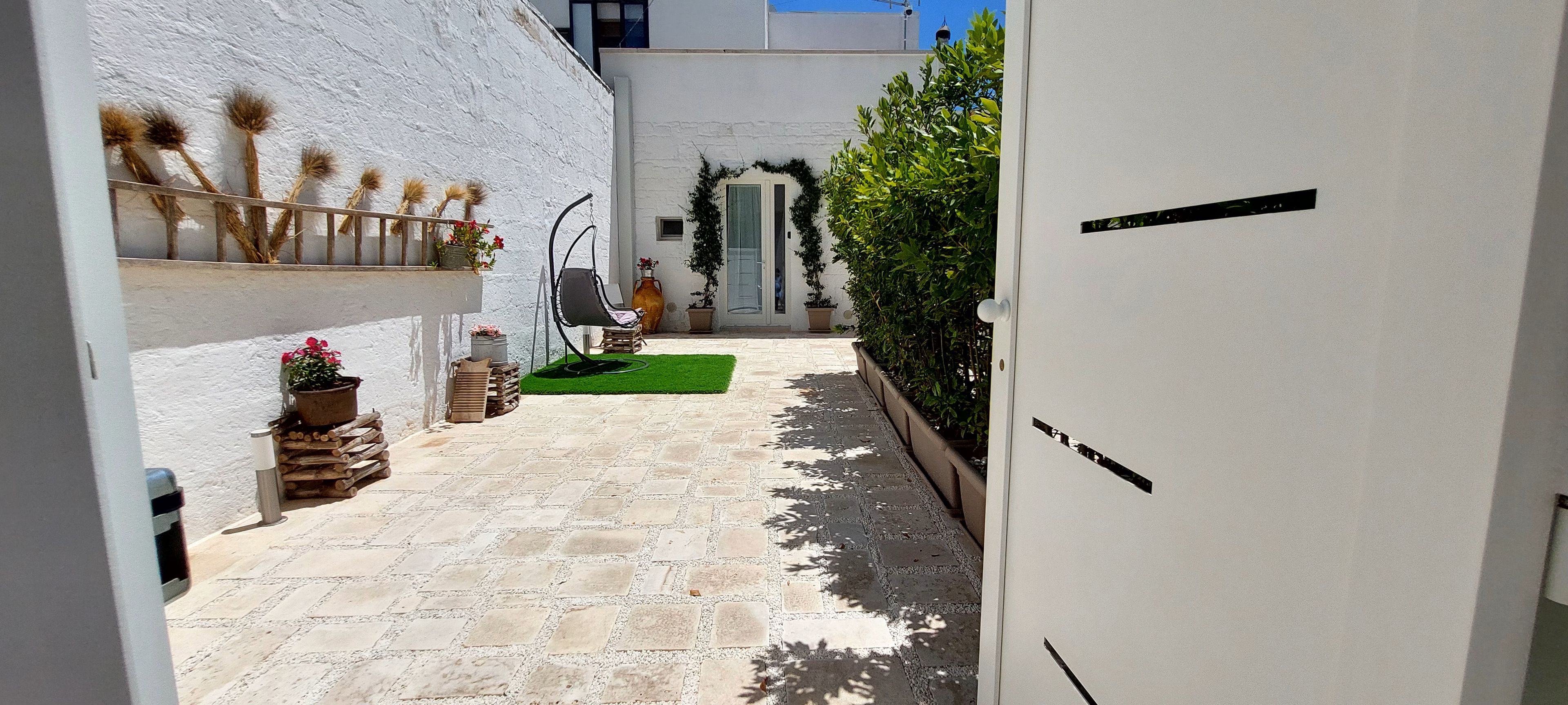 Un cortile stretto con pavimento in pietra, una sedia, piante in vaso e una porta con tenda verde.