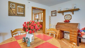 A dining area with a wooden table, chairs, and a vase of red flowers. There is a wooden cabinet with drawers and a shelf above it. - Cozy Fort Cobb Home Rental Near Lake Access! (Fort Cobb)