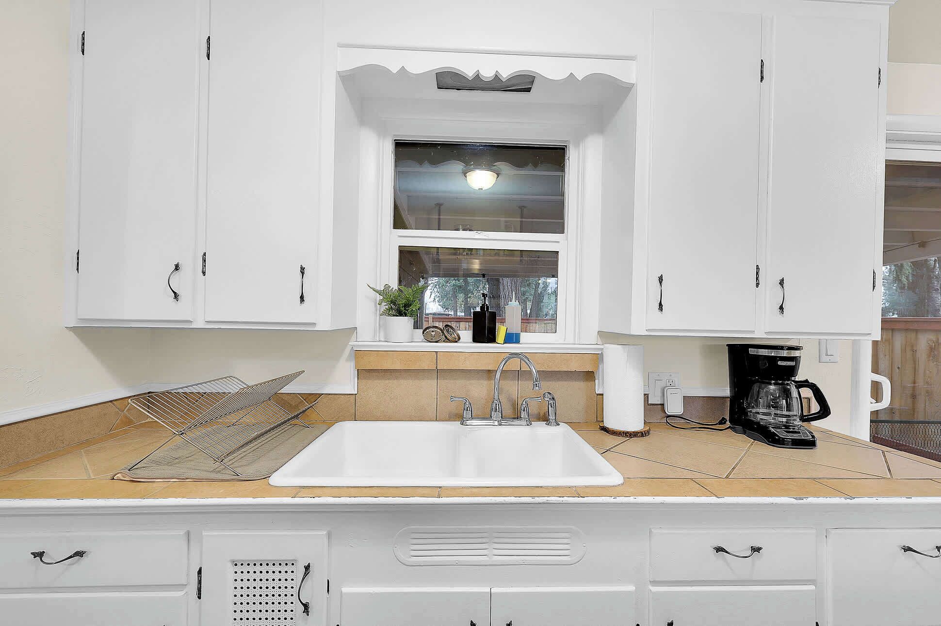 Una cocina con armarios blancos, un fregadero, una ventana y una cafetera.