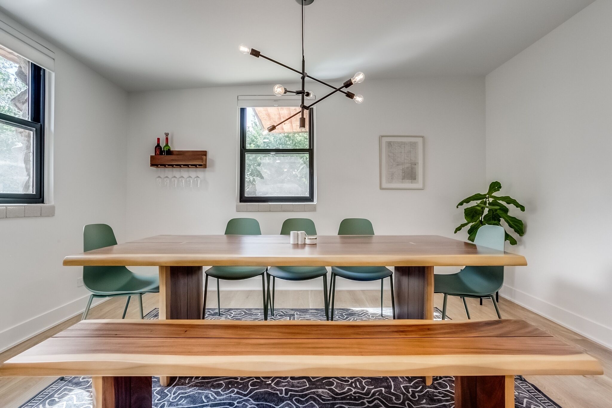 A dining area with a large wooden table, green chairs, a modern pendant light, and a potted plant.
