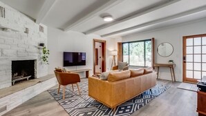 Ein modernes Wohnzimmer mit Kamin aus weißem Backstein, einer großen Couch, einem Fernseher und einem großen Fenster.