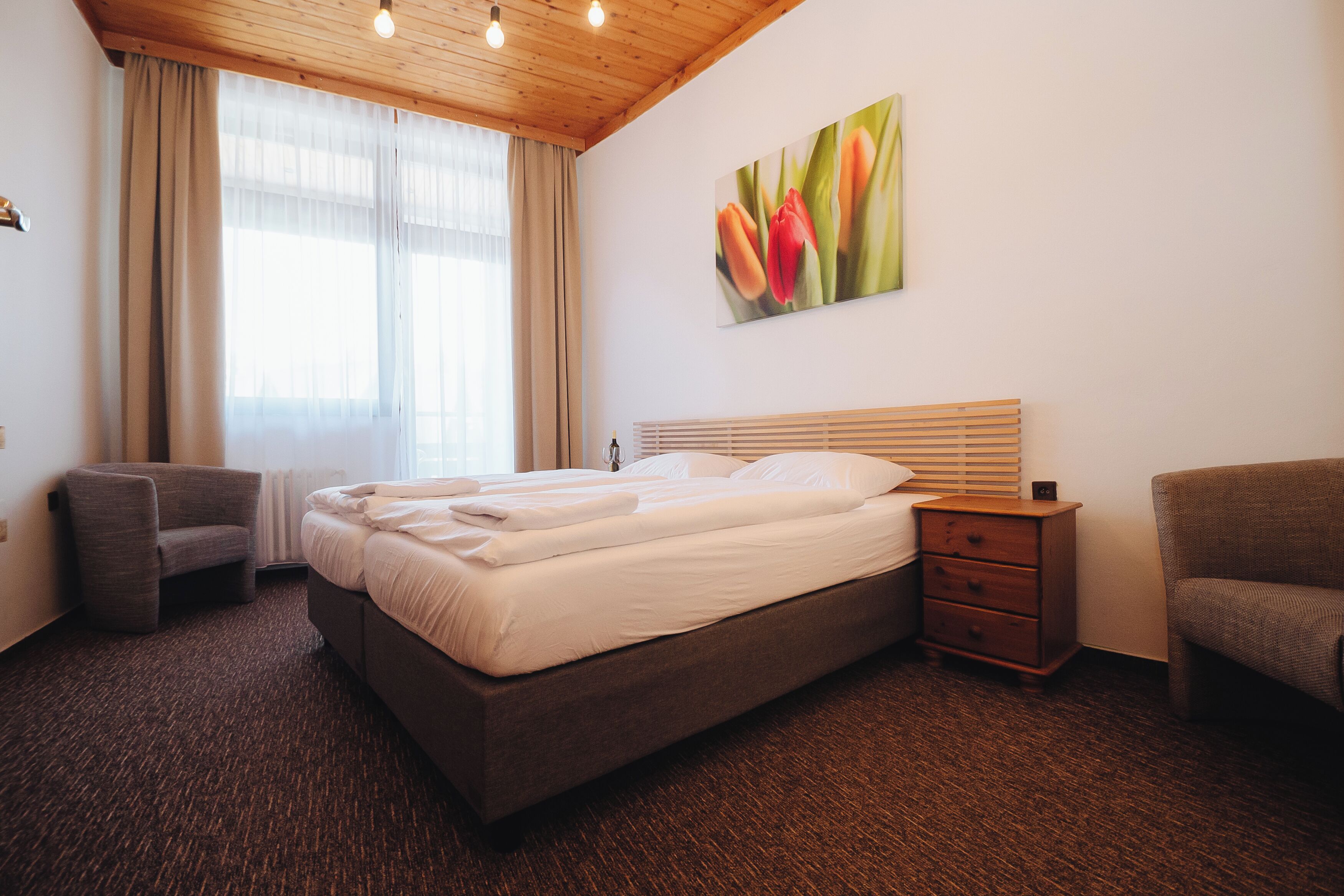 Una habitación de hotel con una cama, una silla, una mesita de noche y un cuadro en la pared.