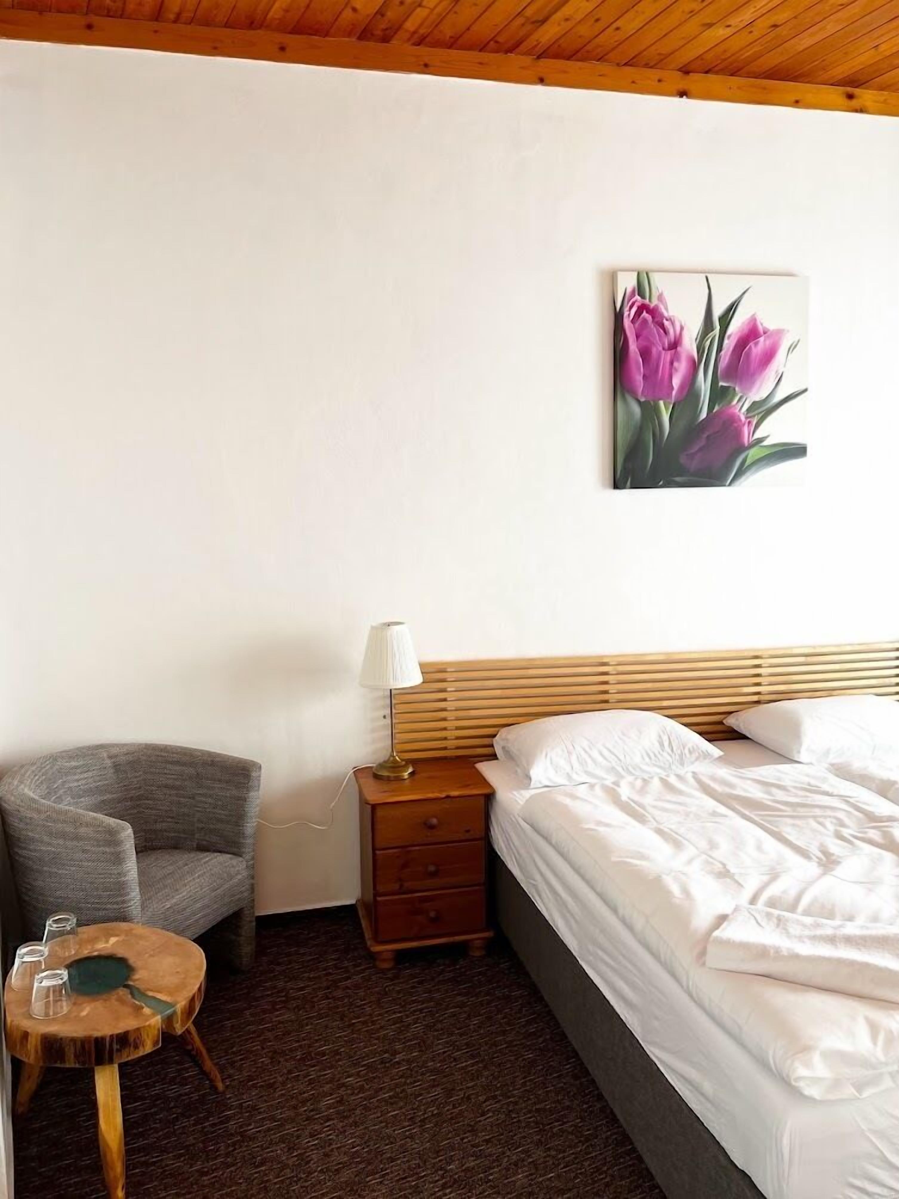 A bedroom with a bed, a chair, a small wooden table, and a nightstand.