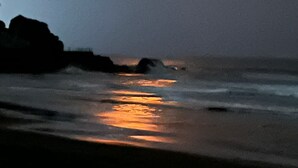 Ein Sonnenuntergang über einem Strand mit Wellen und Felsenformationen.
