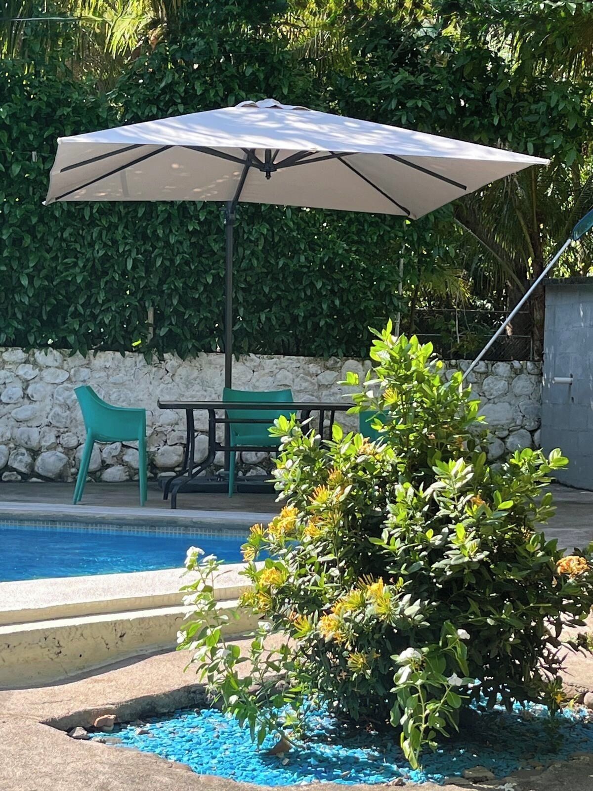 Uma área de piscina com mesa e cadeiras, um grande guarda-sol e uma parede de pedra.