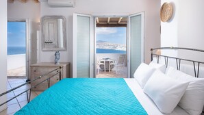 Un dormitorio con cama, cómoda, espejo y vista al mar a través de una puerta abierta.