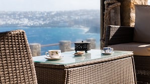 Una silla de mimbre y una mesa con vistas al mar y al paisaje urbano.