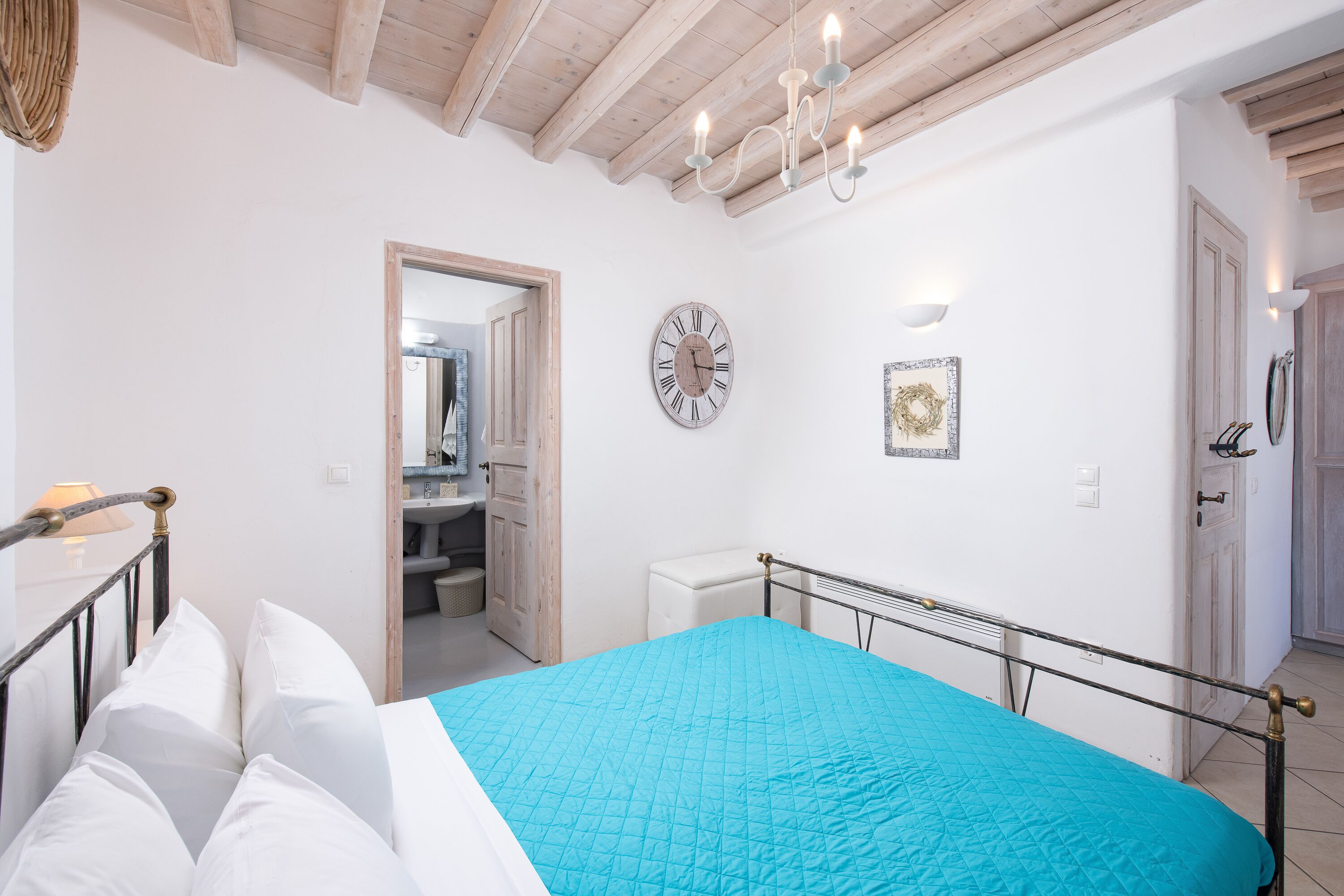 A bedroom with a bed, a clock, a chandelier, and a door.
