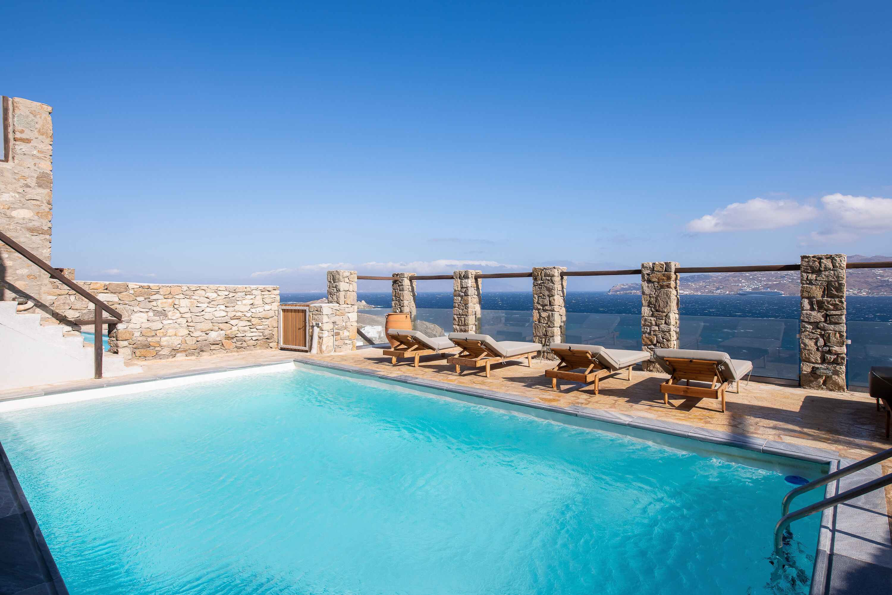 Une piscine bordée de murs en pierre et dotée de chaises longues, offrant une vue panoramique.