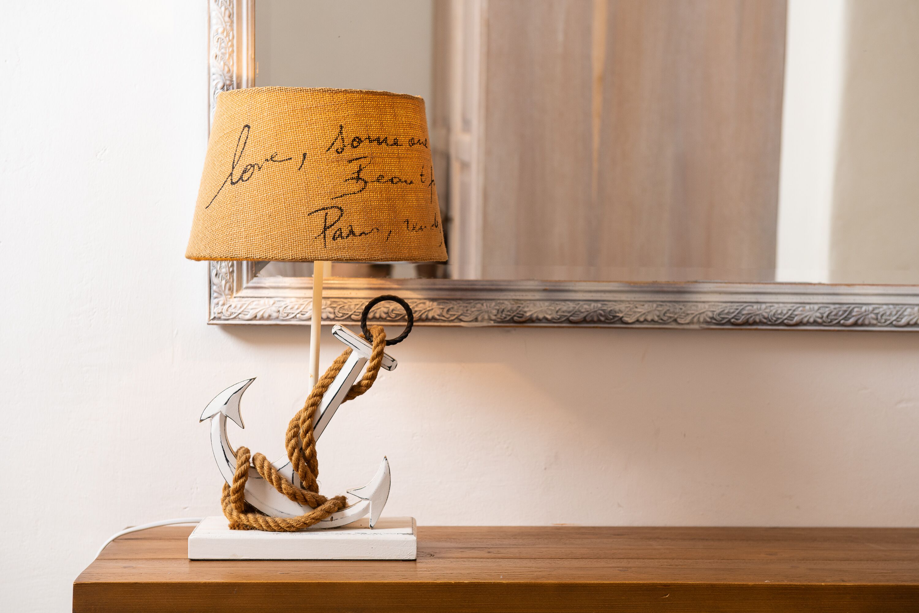 A lamp with a handwritten note on the shade, a decorative anchor, and a mirror on a wooden surface.