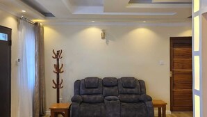 A living room with a dark gray sectional sofa, wooden flooring, and a wooden door. - Astrahill Villa,  A Royal Gateway near Ngong Hill. Nairobi (Kajiado County)