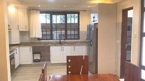 A modern kitchen with white cabinets, a wooden dining table, and a built-in refrigerator. - Astrahill Villa,  A Royal Gateway near Ngong Hill. Nairobi (Kajiado County)