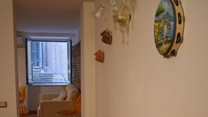Un corridoio con pavimento piastrellato, una piccola zona salotto con una sedia e un tavolo, e un elemento decorativo a parete.