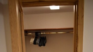 Una stanza con una porta in legno, pavimento piastrellato, un armadio con abiti appesi e un interruttore della luce sulla parete.