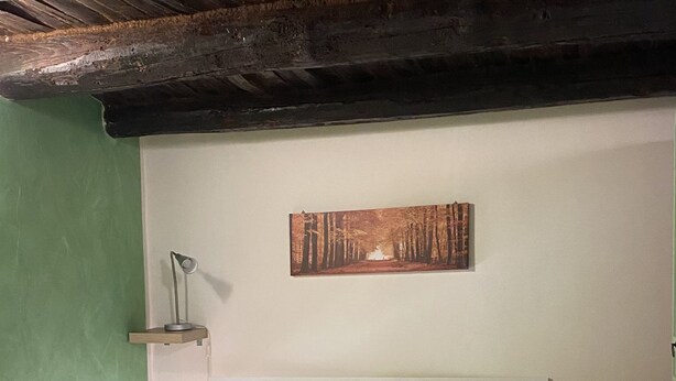 Un letto singolo con copriletto verde in una stanza con pavimento piastrellato e soffitto in legno.