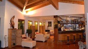 A spacious living area with a wooden ceiling, a bar with stools, and a seating area with sofas. - Hotel Alpina Resort nature & wellness (Wenns)