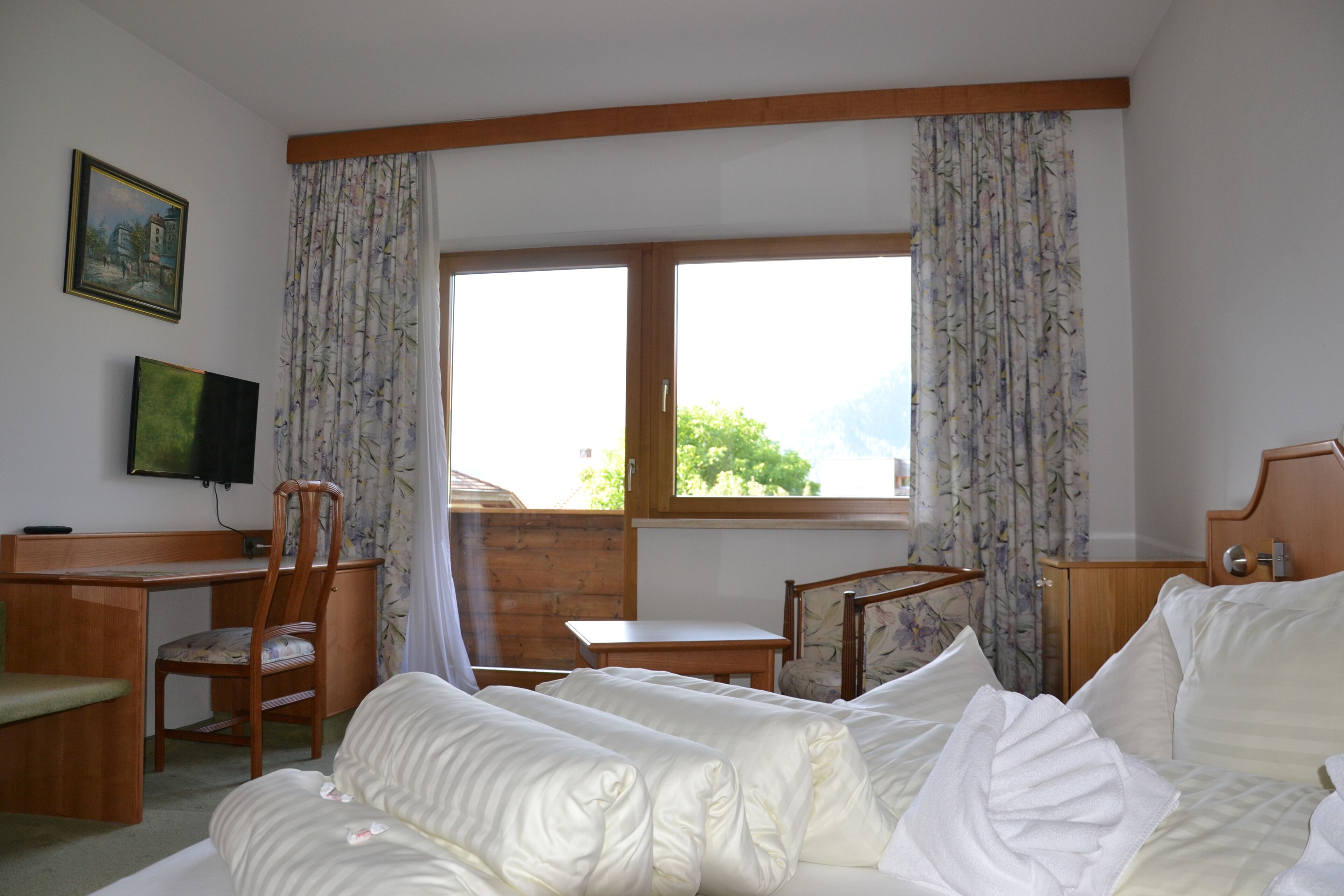 Hotelkamer met een bed, bureau, stoel, televisie en raam met gordijnen.