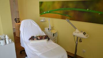 Uma sala de exames médicos com uma cama para pacientes, uma cadeira de dentista e uma pintura pendurada na parede.