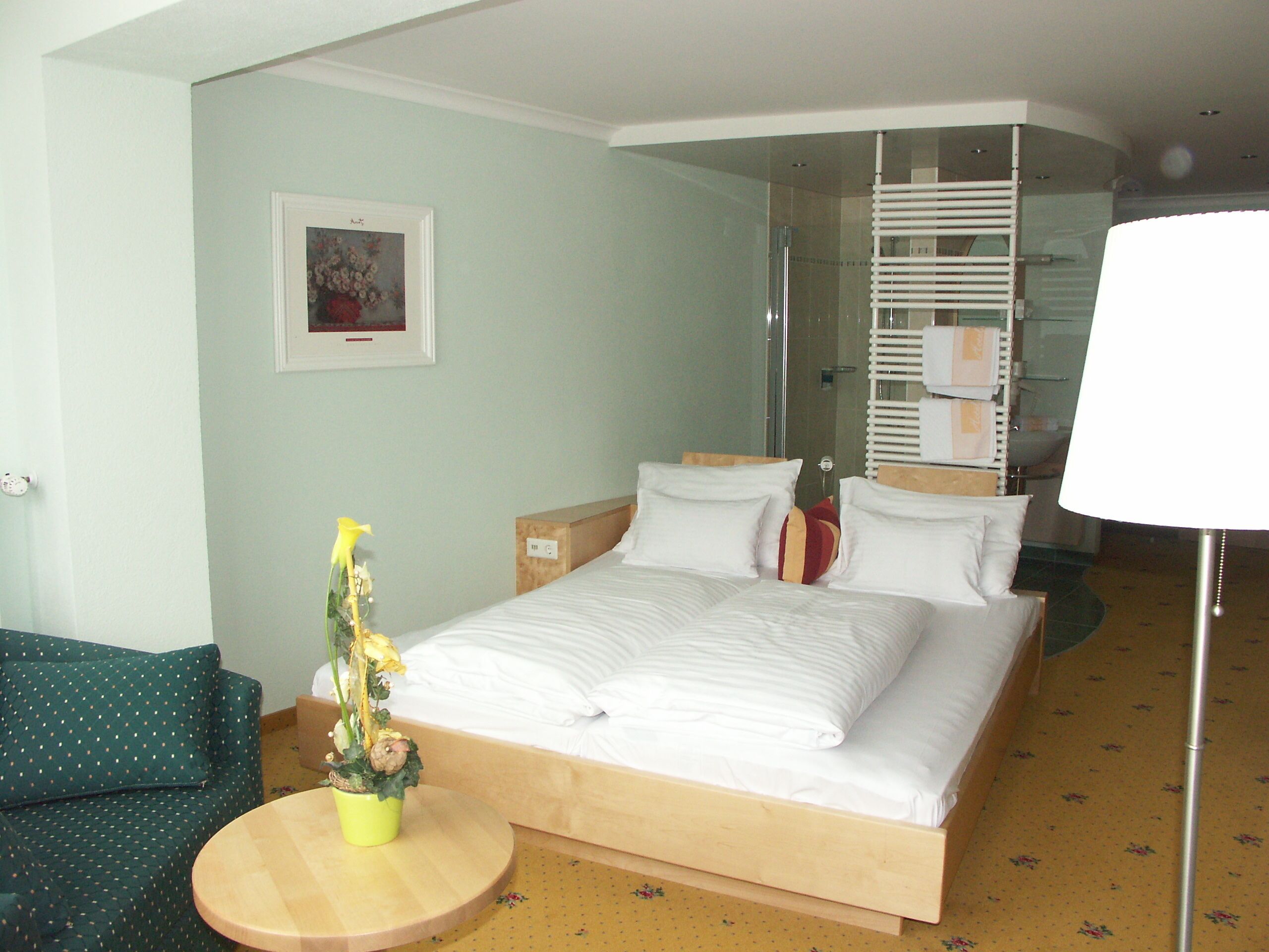 A hotel room with a large bed, a small round table, a sofa, a shower area, and a framed picture on the wall.