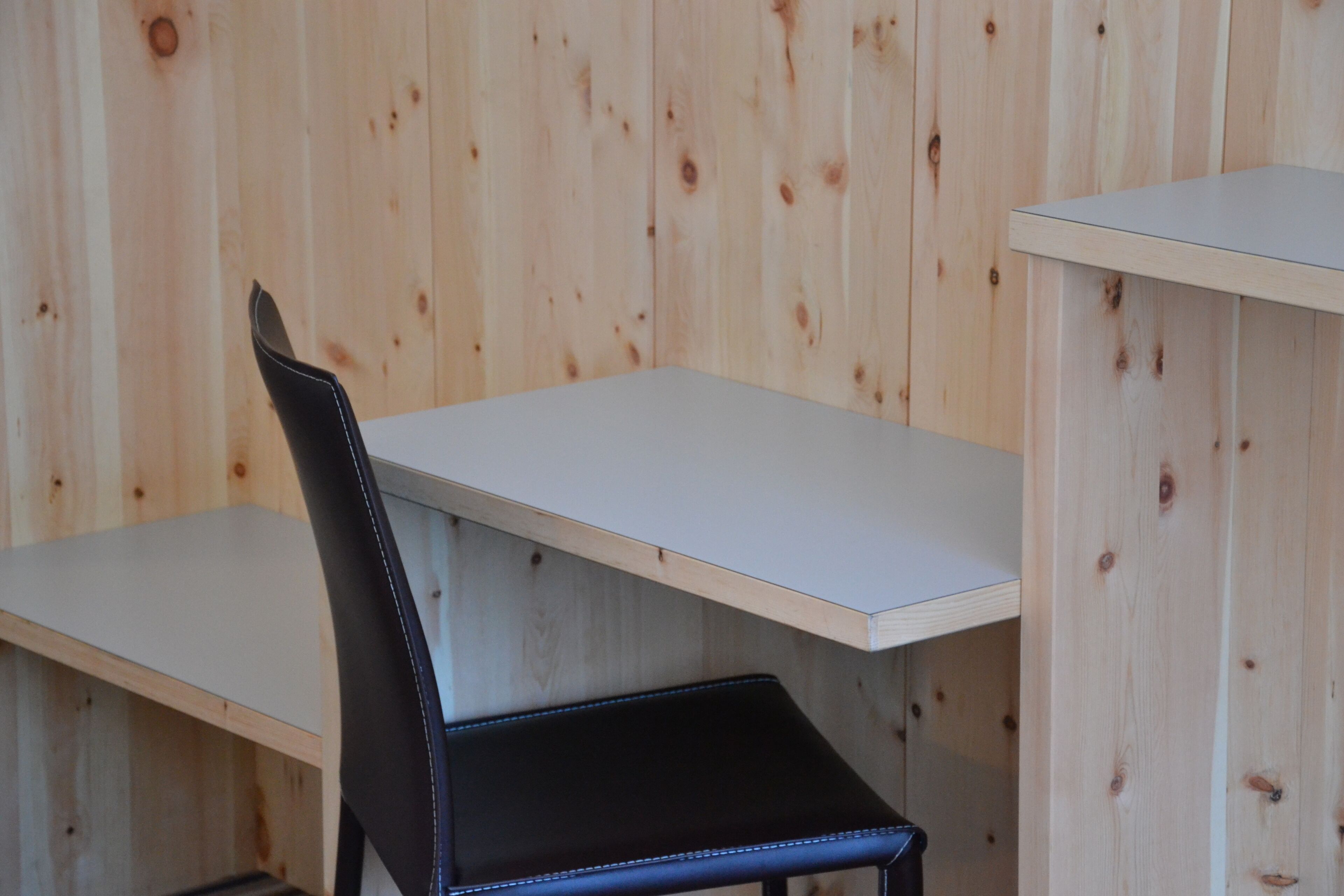 A room with a wooden wall, a black chair, and a white table.