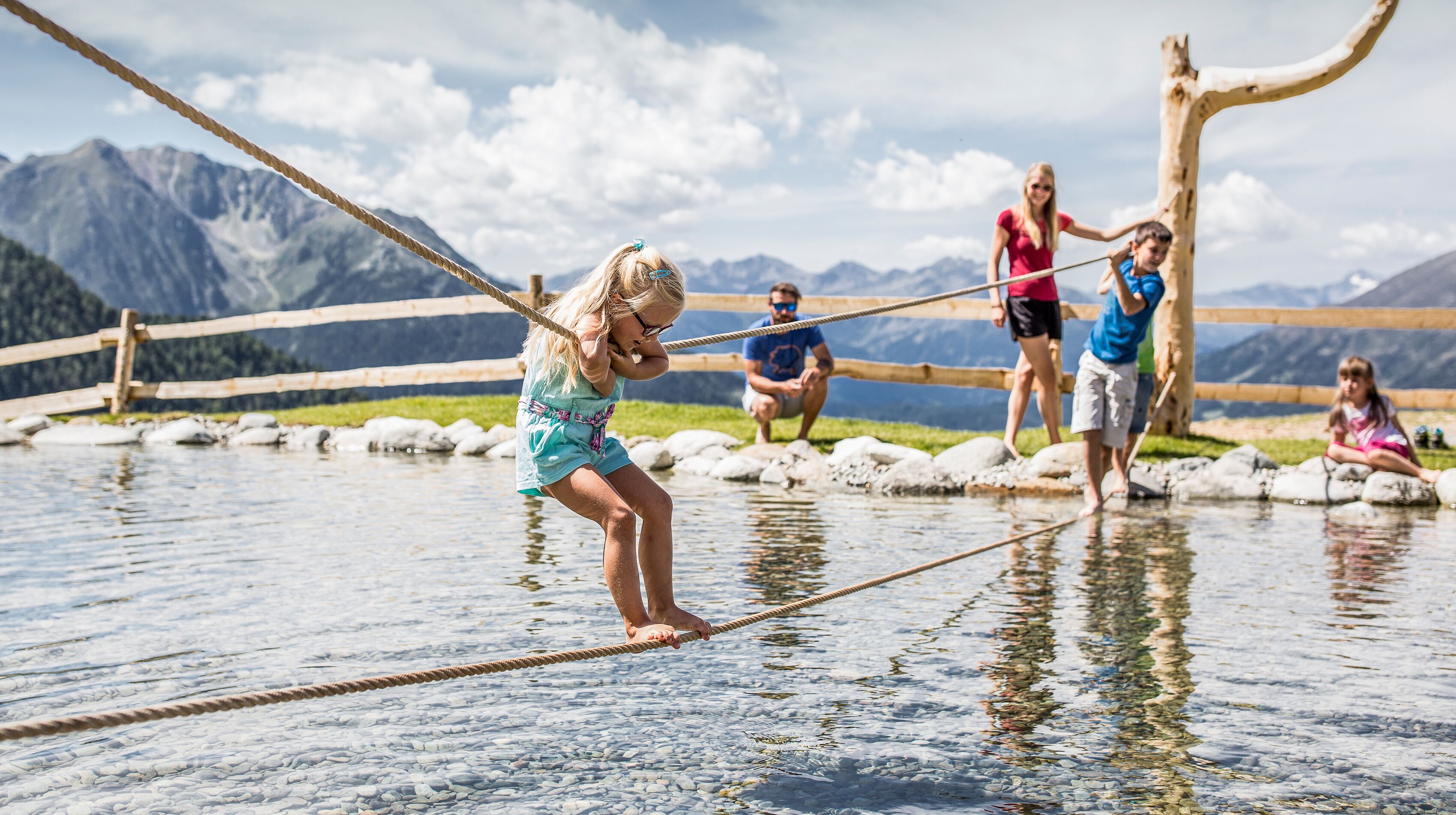 Eine Seilbrücke über ein Gewässer, im Hintergrund Berge.