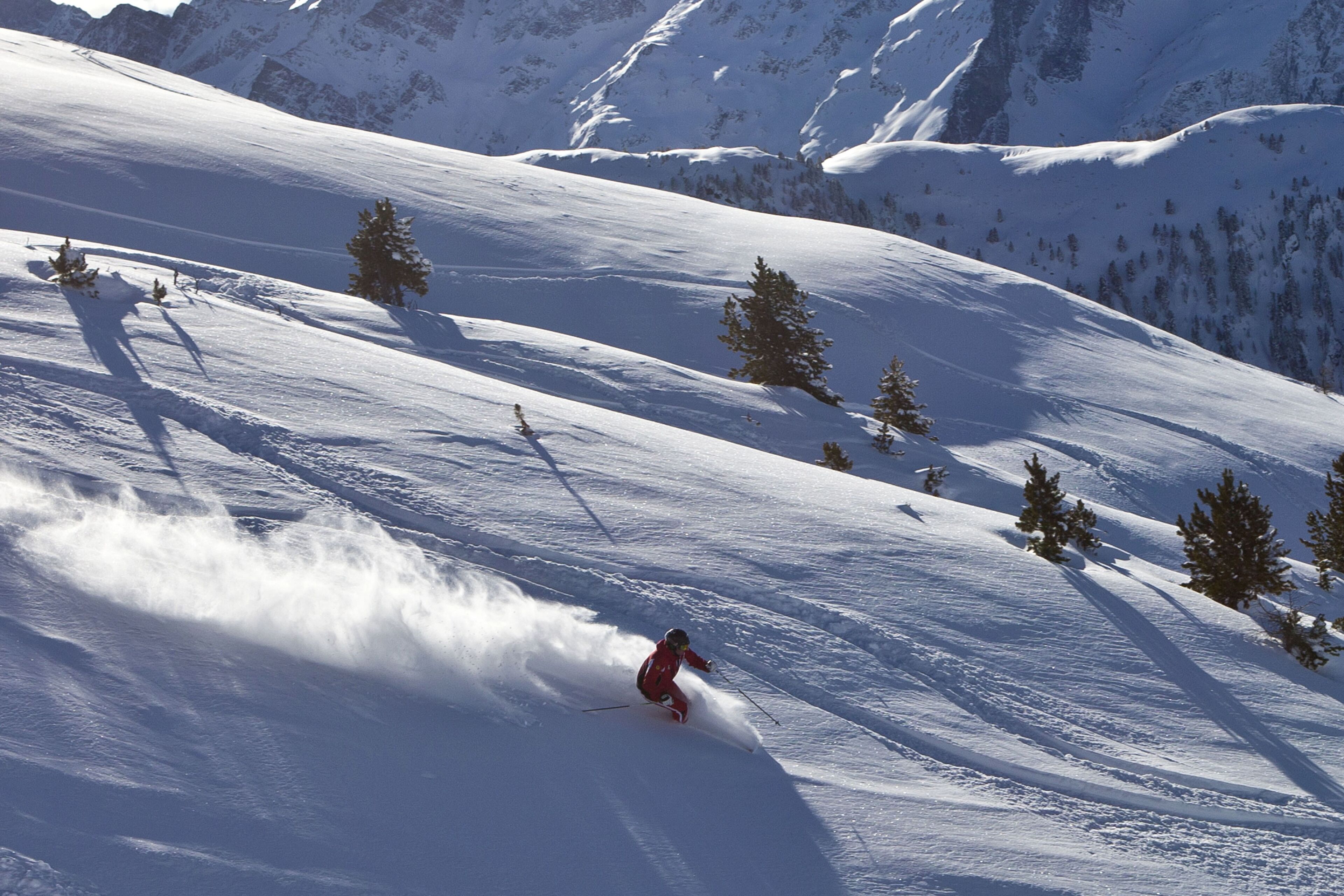 Eine verschneite Berglandschaft, ein Skifahrer fährt einen Hang hinab.