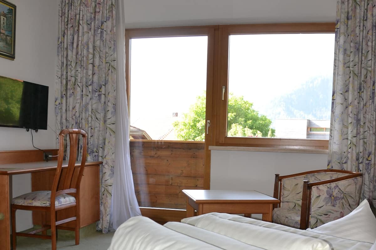 Une chambre d’hôtel avec un lit, deux chaises, un bureau et une fenêtre donnant sur les montagnes.