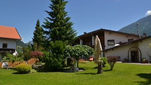 A house with a red roof, a large evergreen tree, and a lawn. - Hotel Alpina Resort nature & wellness (Wenns)
