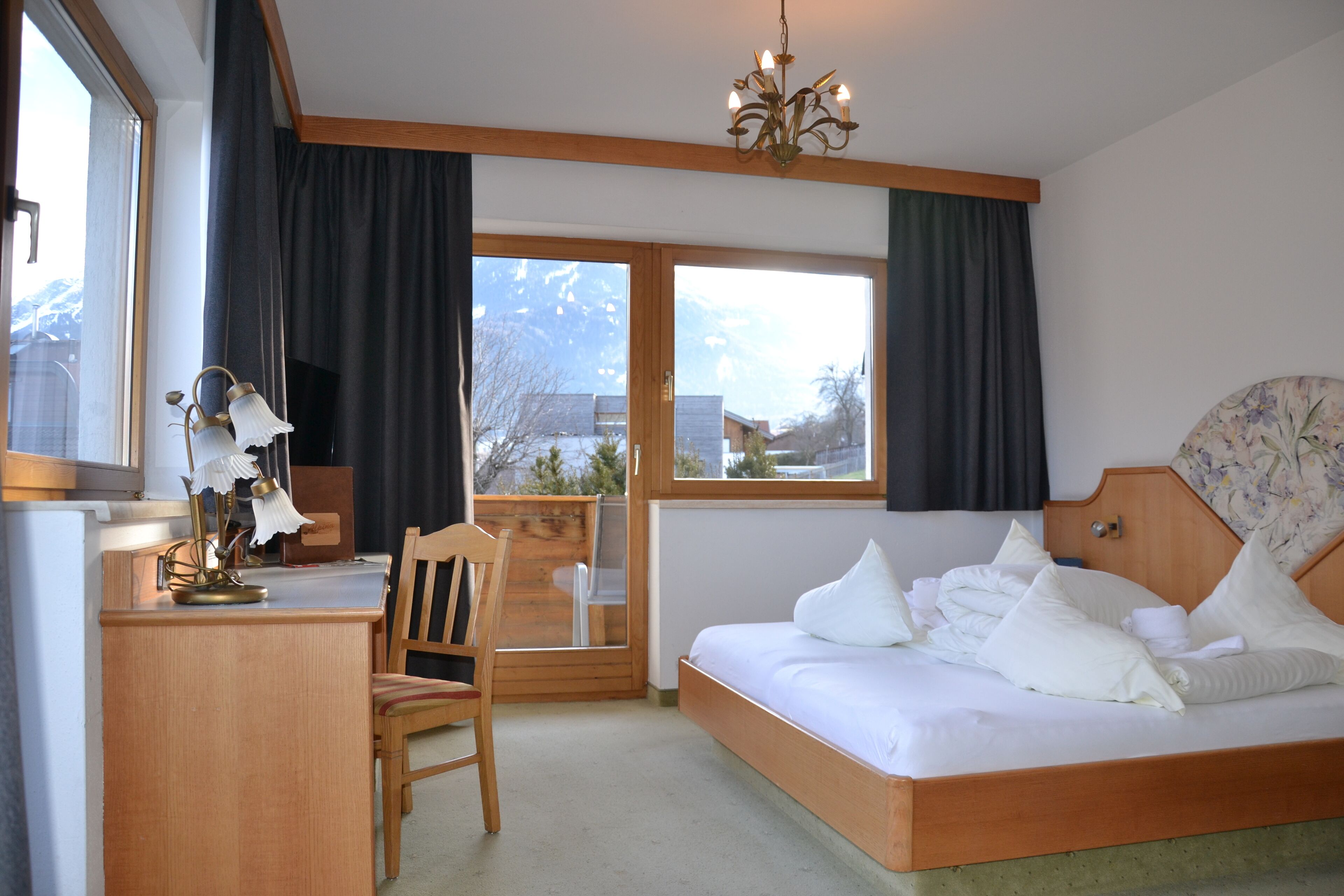 Une chambre à coucher comprenant un lit, un bureau, une chaise, une lampe de bureau et une fenêtre avec des rideaux.
