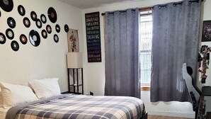 Un dormitorio con una cama, una pared llena de discos de vinilo, un cartel motivacional y una ventana con cortinas.