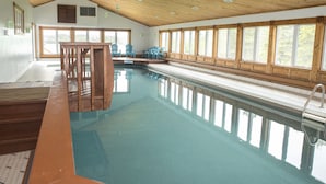 Une piscine avec une terrasse en bois et des chaises, de grandes fenêtres et un plafond en bois.