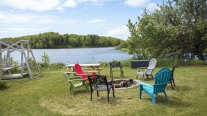 Un espace extérieur aménagé avec des chaises Adirondack et une balançoire, le tout situé près d’un lac.