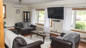 Un salon avec un canapé, des fauteuils, une table basse, un téléviseur et une horloge au mur.