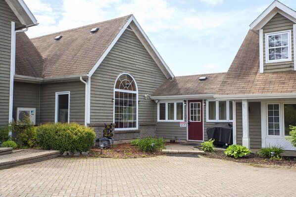 A two-story building with a gabled roof, a covered porch, and a red door.