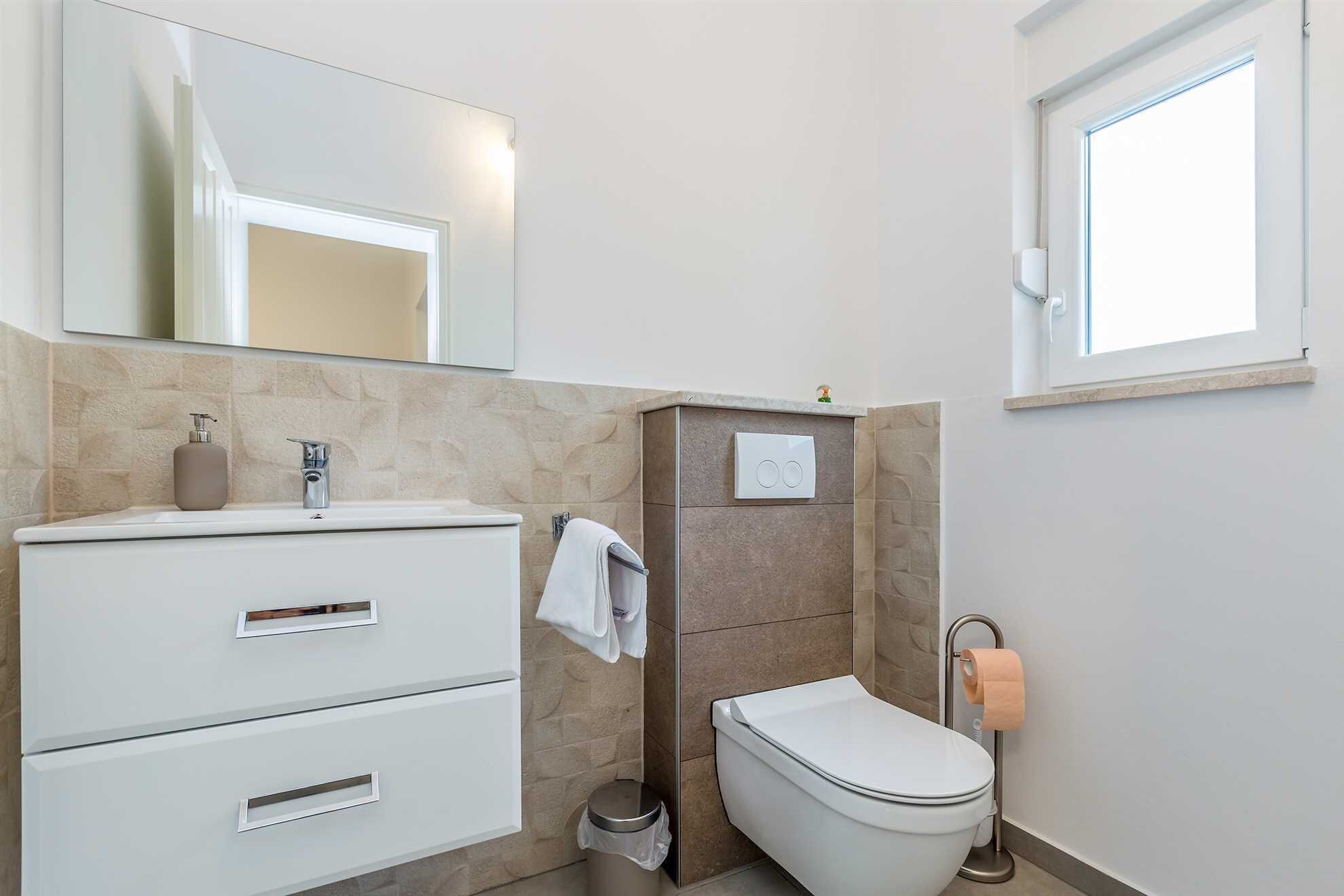 Un baño moderno con tocador blanco, inodoro y ventana.